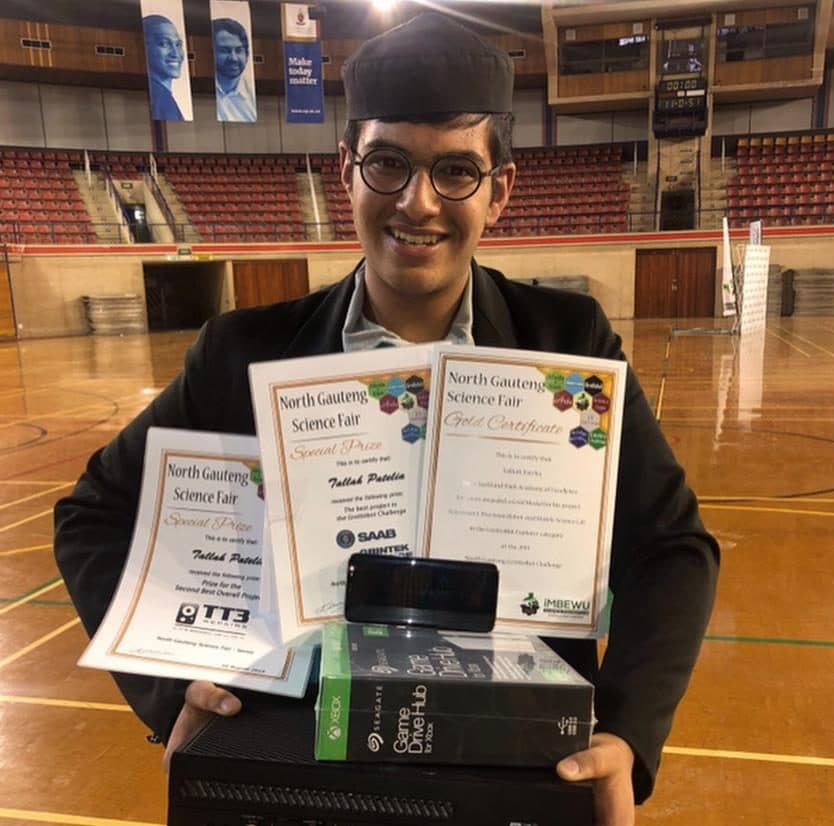 Talhah Patelia holding his North Gauteng Science Fair certificates in a sports hall
