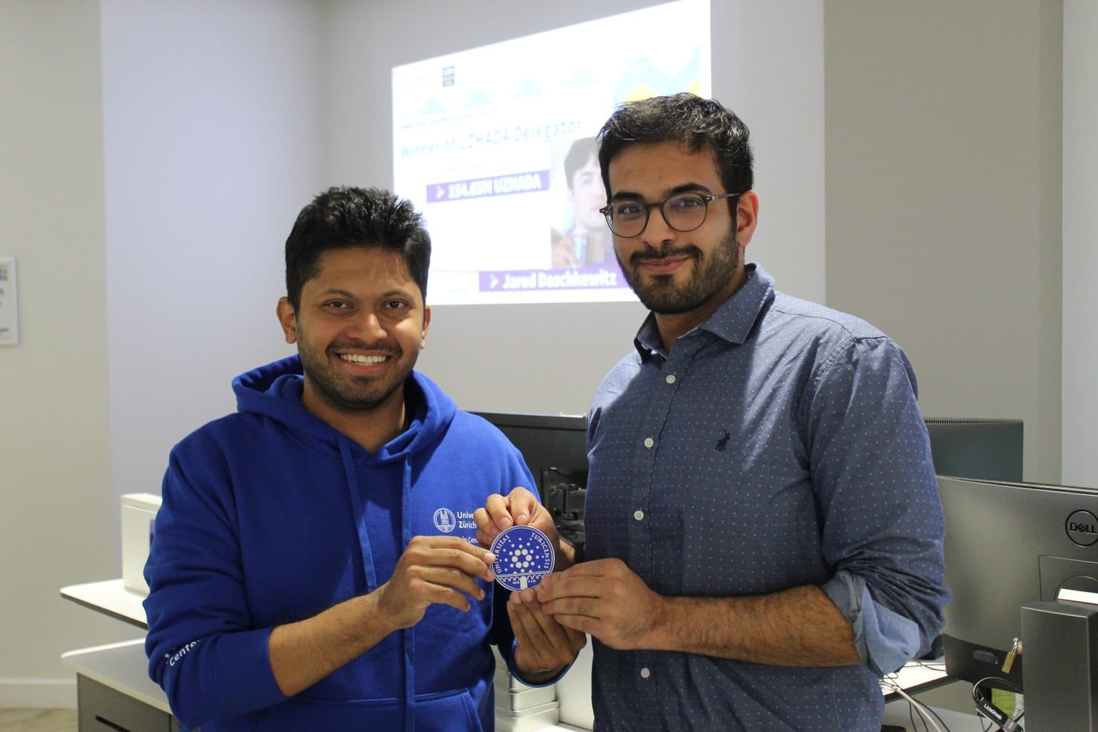 Talhah Patelia, on the right, standing with a man in a blue hoodie while they hold a small badge