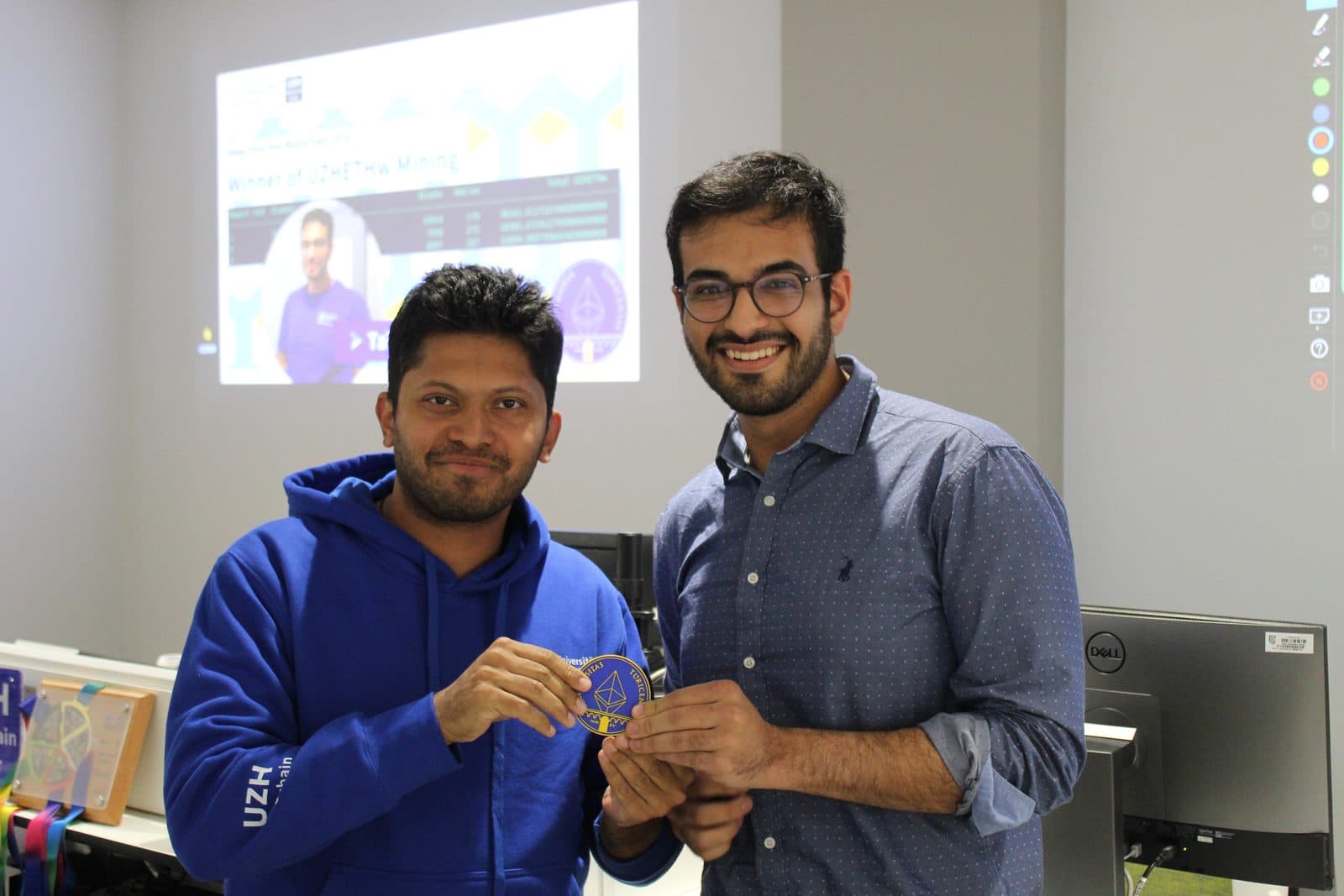 Talhah Patelia, on the right, standing with a man in a blue hoodie while they hold a small badge