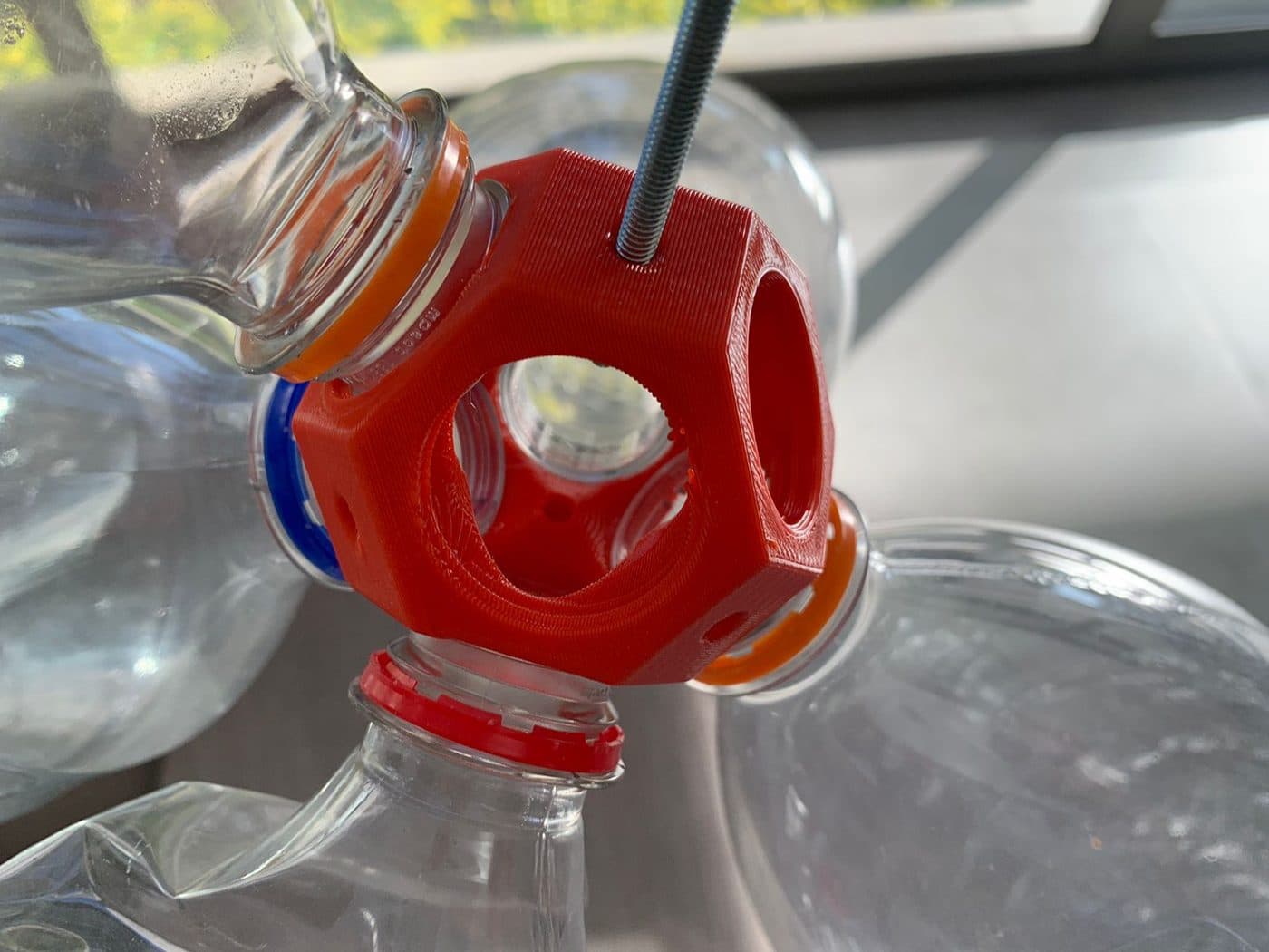 An orange connector holding several plastic bottles together with a rod through it