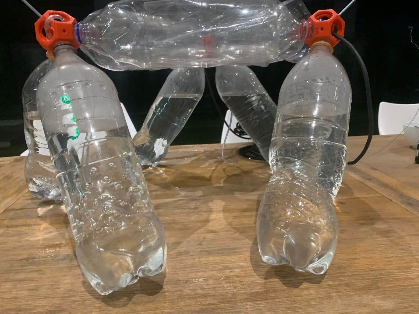 A small frame built from plastic bottles joined by orange connectors, standing on a wooden table