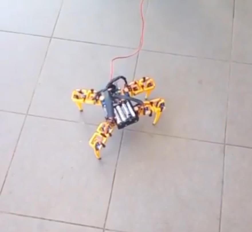 A small yellow quadruped robot walking on a tiled floor